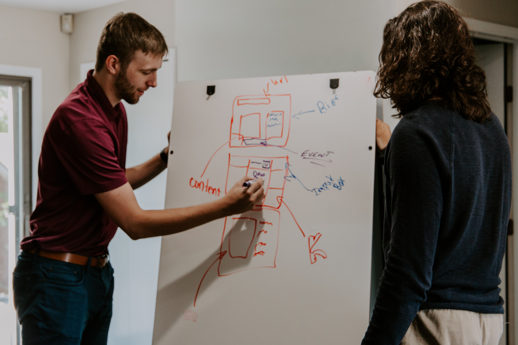 Two people reviewing diagrms written on a white board