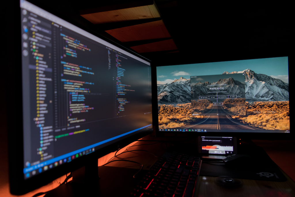 Two black flat screen computer monitors. First monitor displays a text editor and the second displays a website